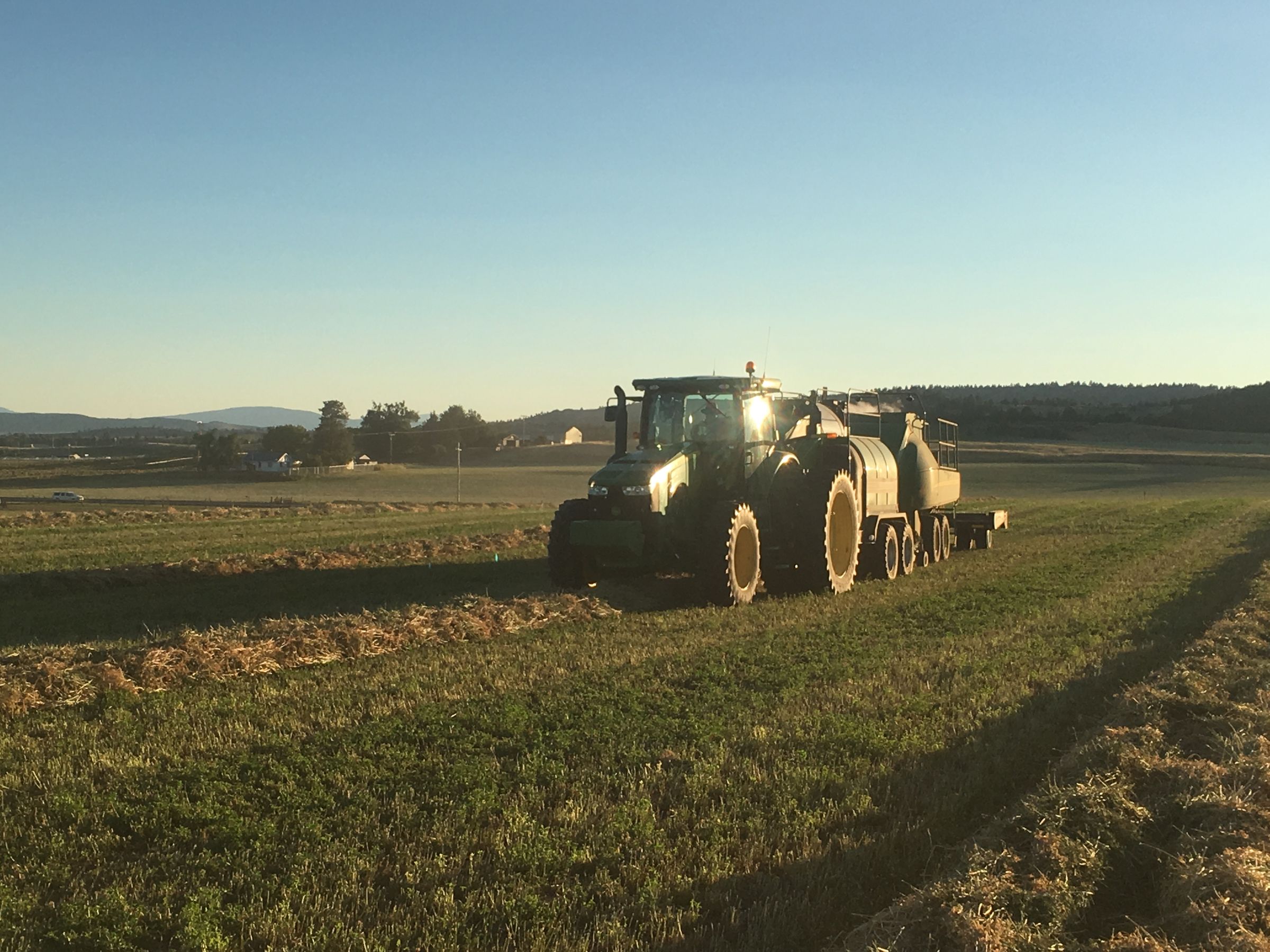 A Shasta Seed tractor pulling nutrient tanks through a field at sunset